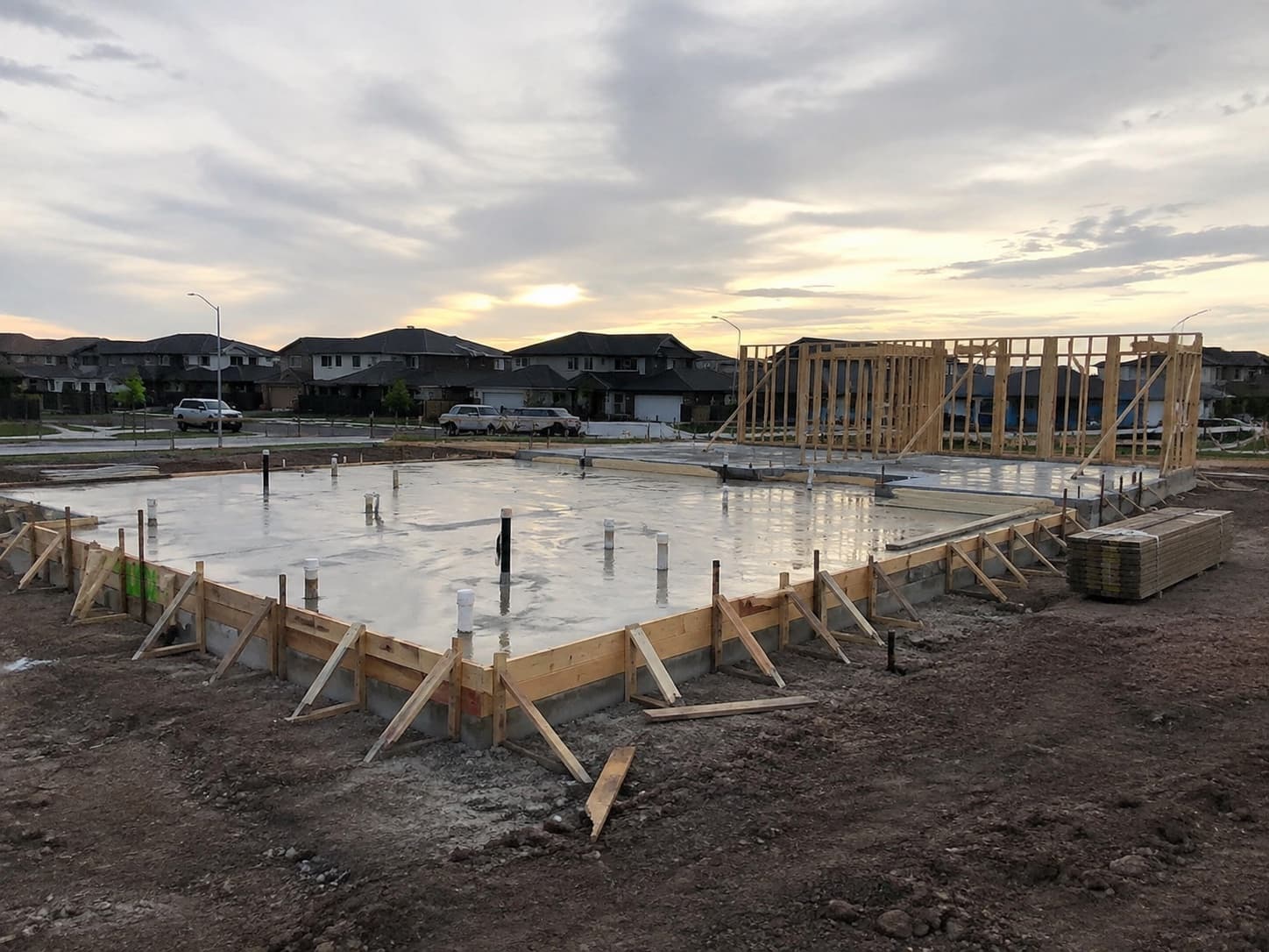 Cured residential slab foundation with forms still in place and the first exterior walls framed and braced at sunset